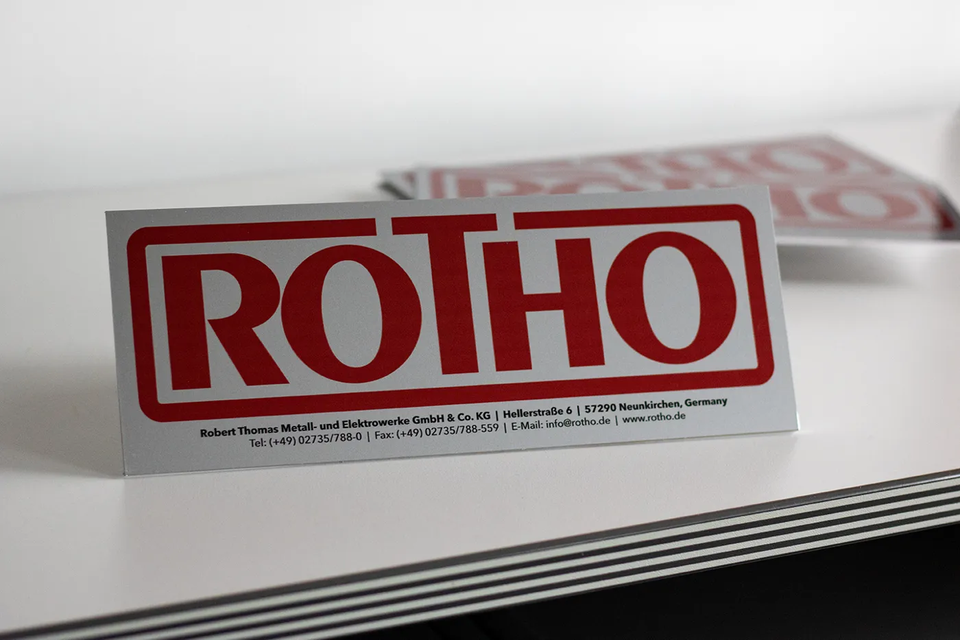 Firmenschild von Rotho auf silbernem Aluminium als Tischaufsteller